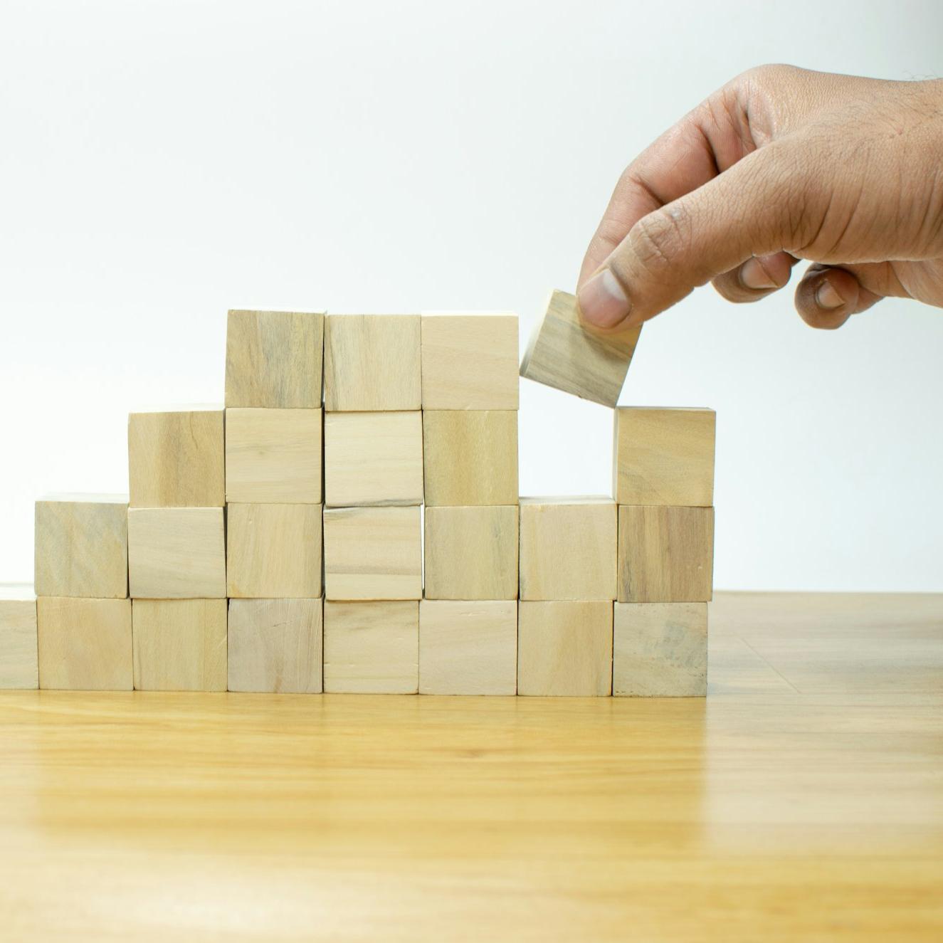 A person placing a block into a pile of wooden blocks
